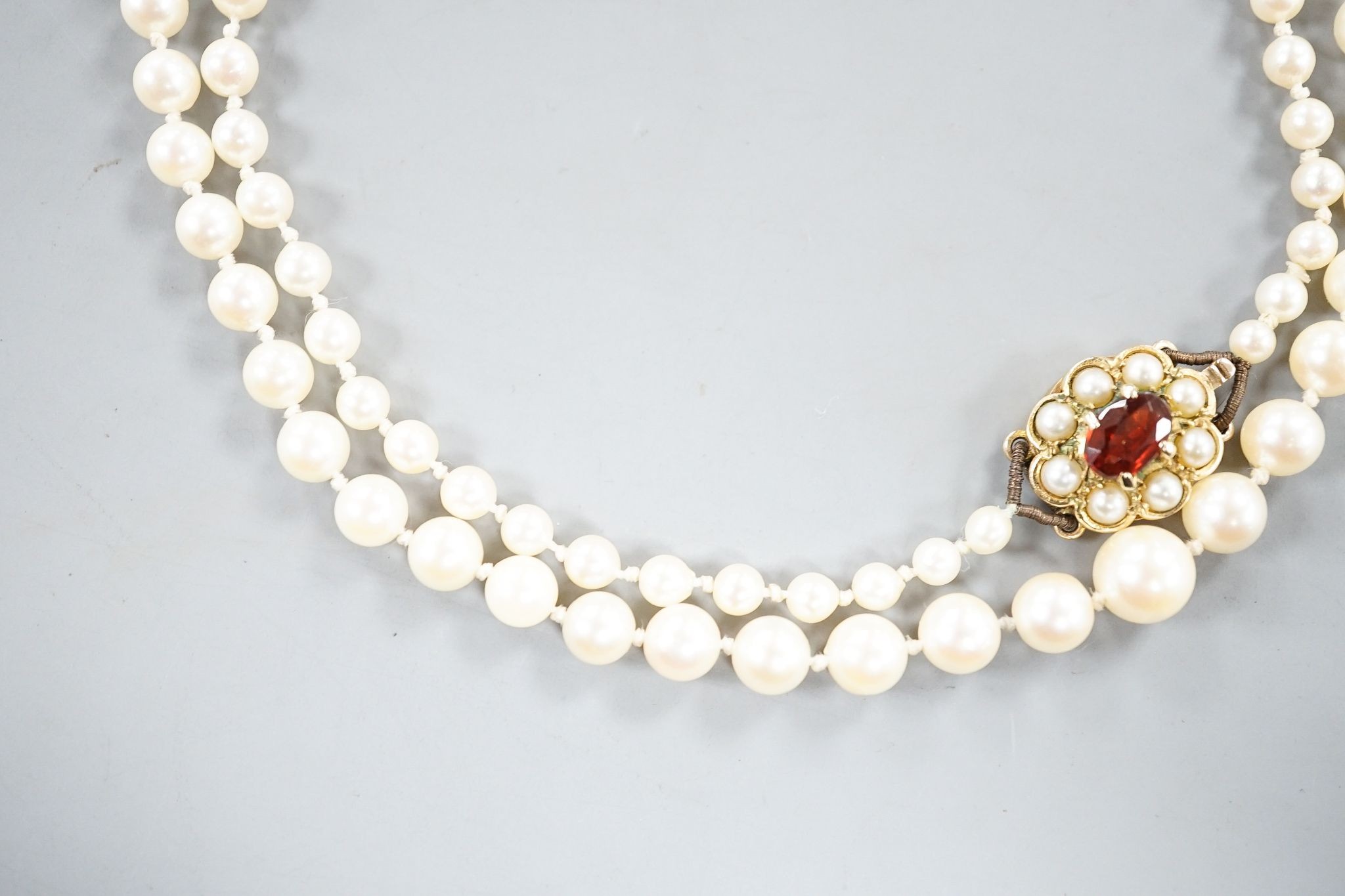 A single strand graduated cultured pearl necklace, with 9ct, garnet and cultured pearl cluster set clasp, 53cm.